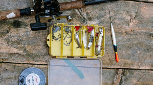 Open tackle box with fishing lures and hooks alongside a fishing rod showing essential fishing gear