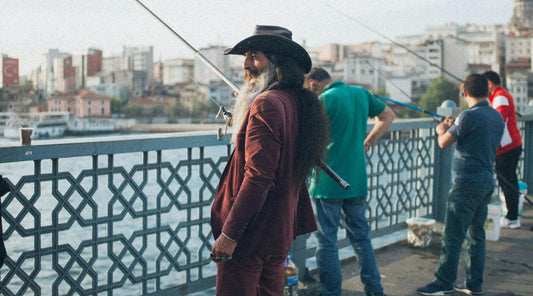 Man wearing stylish fishing fashion with a hat and suit while fishing on a city waterfront